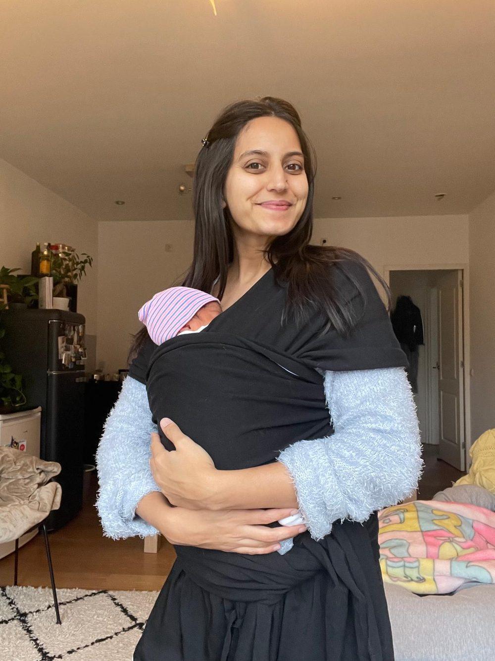 A smiling mother carrying her newborn baby in a wrap