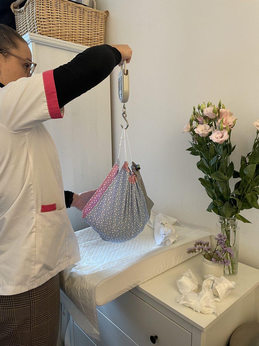 A maternity nurse weighing a newborn baby in a hanging scale
